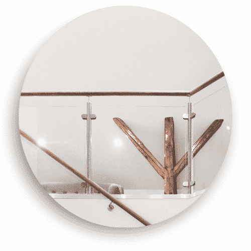 Ett inomhusräcke i glas med rostfria stolpar och en överliggare i trä. Räcket omger en öppen yta, där en dekorativ trädetalj bidrar till en varm och naturlig känsla i inredningen.