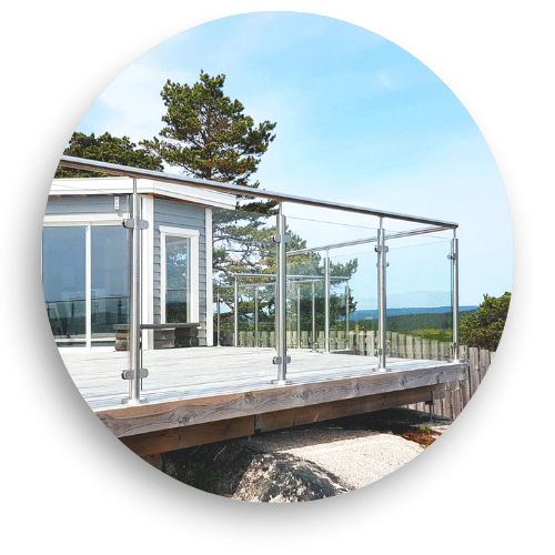 Glasgeländer aus Edelstahl mit Klemmbefestigungen auf Holzdeck – runde Handlauf und Blick aufs Meer im Hintergrund.