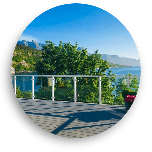 Terrasse avec garde-corps en verre et montants blancs, offrant une vue panoramique sur le fjord et les montagnes.