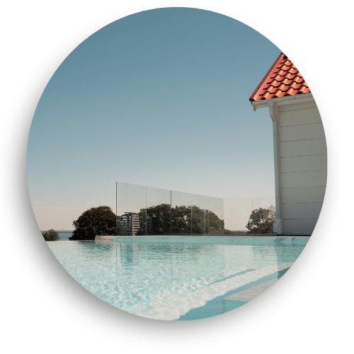 Stilrent glasräcke utan stolpar runt pool, ger obruten utsikt och elegant inramning mot landskap och horisont.