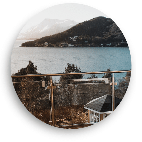 Glass railing with stainless steel posts, clamps and top rail, framing views of water, forest and mountains with a sleek, natural look.