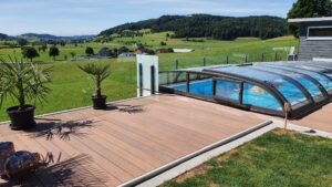 Glass Pool Fencing with Retractable Pool Cover Defined pool area with modern glass balustrade, retractable pool cover and timber decking in a rural setting with rolling green hills.