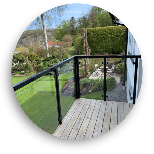 Elegantes Glasgeländer mit schwarz beschichteten Aluminiumprofilen auf Holzterrasse in grüner Gartenlandschaft.