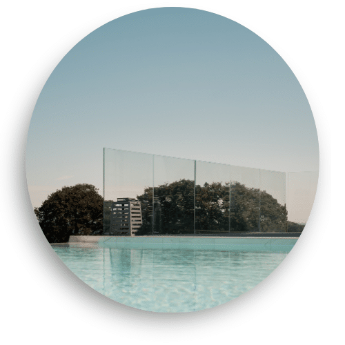 Pfostenloses Glasgeländer mit Bodenprofil am Pool – freie Sicht auf die Landschaft, Wasser reflektiert den Himmel.
