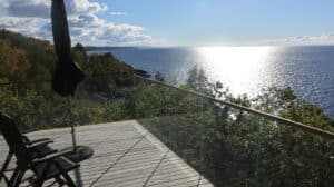 Glasværn med træhåndliste på kystterrasse Hjørnemonteret glasværn med træhåndliste og panoramaudsigt over skov og hav fra terrasse.