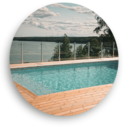 Glasstaket med aluminiumstolpar runt träbelagd pool, kombinerar säkerhet med fri sikt över sjölandskap.