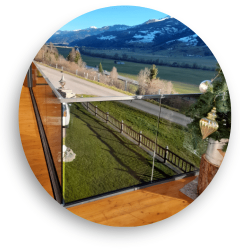 Pfostenfreies Ganzglasgeländer auf Holzterrasse montiert, mit freiem Blick auf Landschaft und schneebedeckte Berge.
