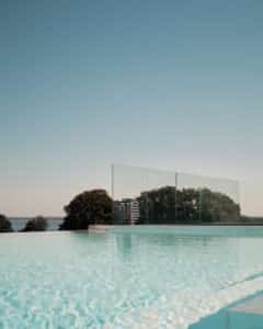Frameless Pool Glass Balustrade Facing the Ocean Premium frameless glass pool fencing around infinity pool with mirror-like water surface and unobstructed forest and ocean views.