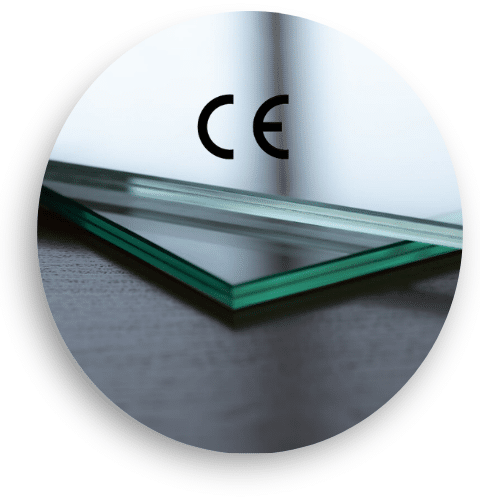 Close-up of two glass panels with green edges resting on a dark surface. The CE mark is visible in the glass reflection, showing compliance with European safety standards. Laminated safety glass provides high strength and shatter protection.