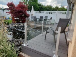Glass Fence with White Posts by Patio and Garden Pond Sleek glass balustrade with white aluminium posts surrounding a small pond and outdoor seating area with red maple trees and classic white fencing.