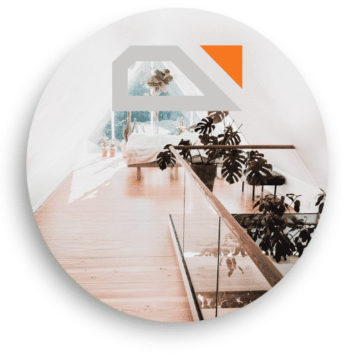 Inomhusbild som visar ett glasräcke med trädetaljer vid ett loft. Räcket sträcker sig längs den träklädda golvet, och vyn från fönstret släpper in naturligt ljus som ger ett ljust och luftigt intryck. Flera växter pryder rummet, vilket skapar en harmonisk och grönskande atmosfär.