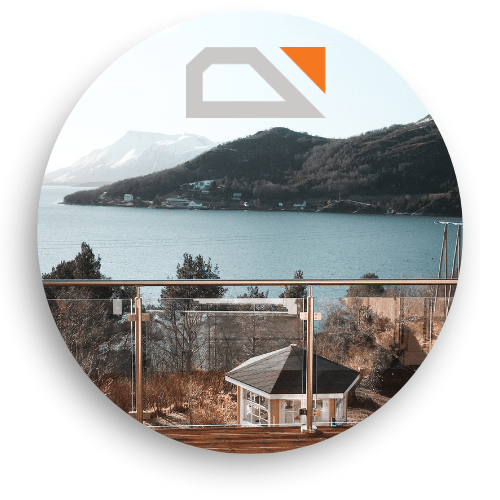 Glasgeländer mit Edelstahlpfosten und Handlauf auf Terrasse mit Panoramablick über Wasser, Berge und Dorf.
