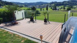 Terrasse med frostet og klart glassrekkverk rundt bassengområde, kombinert med palmer og fri utsikt over landskapet.