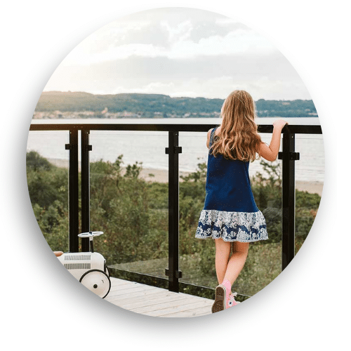 Fille regardant l’horizon derrière un garde-corps noir avec verre, installé sur un balcon avec vue sur la mer.