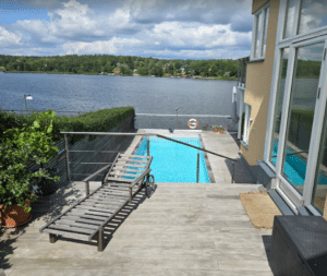 Wiregelænder i rustfrit stål omkring trætarrasse og pool med søudsigt – diskret og sikkert gelænder til terrasse med niveauforskel.