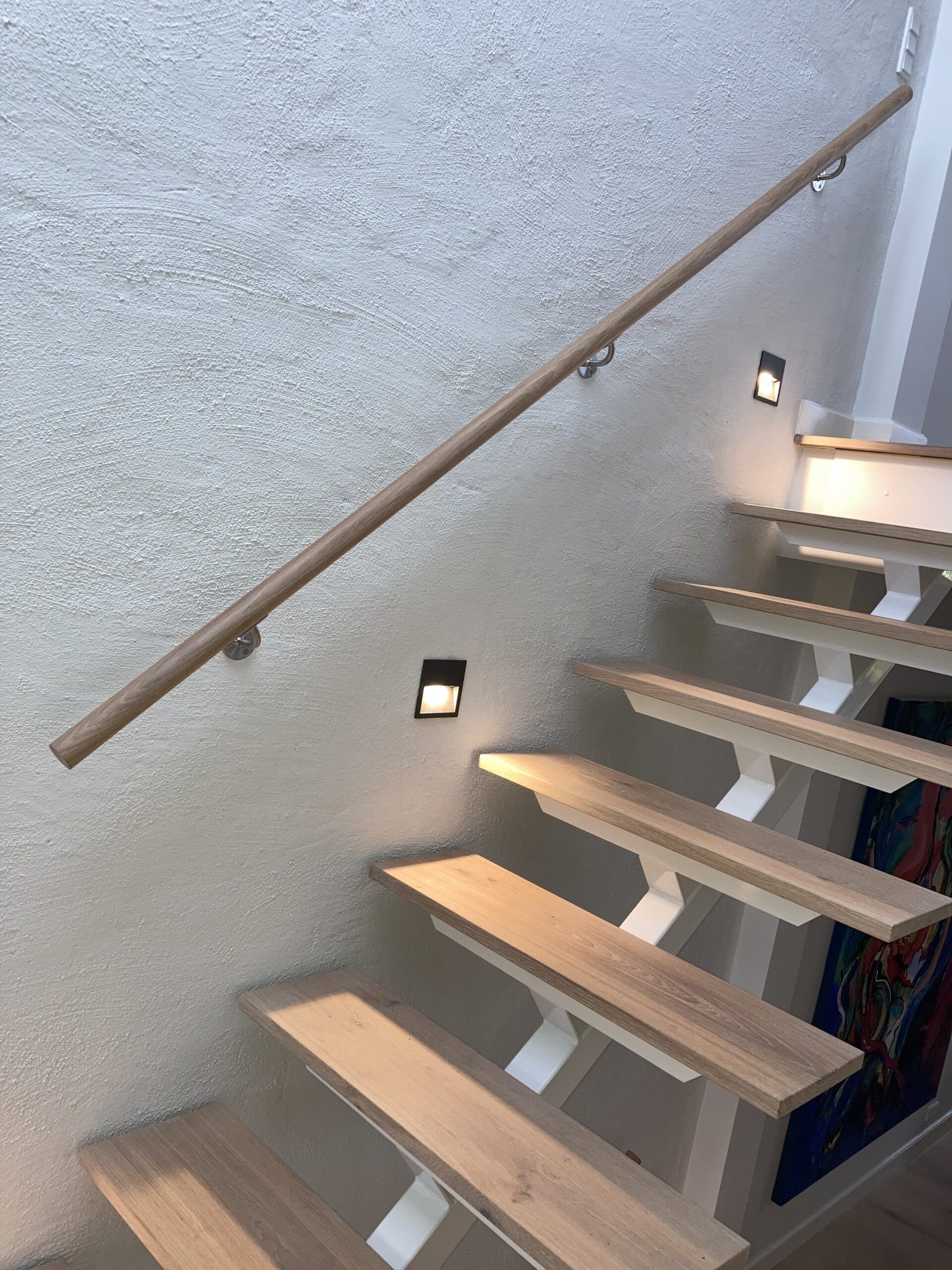 Elegant træhåndliste på væg i lys indendørs trappe med integreret lys og hvide vægge.