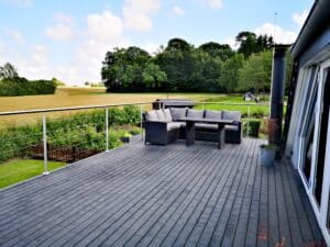 Terrasse mit Edelstahlgeländer und Drahtseilen, grauem Terrassenboden und Sitzgruppe mit Blick über Felder und Landschaft.