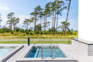 Frameless glass pool fence with sea and spa view Stylish glass railing by spa pool with sea view and green landscape, mounted with discreet black steel posts for safety and elegance.