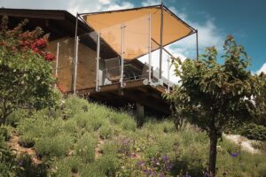 Tall stainless steel balustrade with shade sail Elevated timber deck with stainless steel glass balustrade and sail shade, overlooking lush, sloped garden landscape.