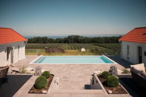 Moderne stolpefrit glashegn omkring infinitypool med udsigt over hav, æbleplantage og åbent landskab.