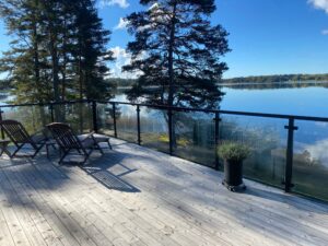 Lakeside black glass railing with open view Sleek black aluminium and clear glass railing on deck by lake, with tree backdrop and open natural surroundings.