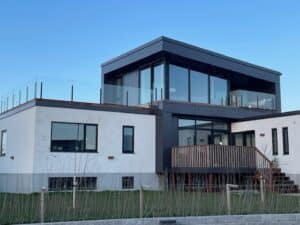 Pfostenfreies Glasgeländer rund um eine Dachterrasse eines modernen Hauses mit großen Fensterflächen und minimalistischer weiß-schwarzer Fassade.