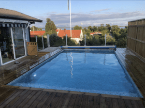 Glassrekkverk i hvit aluminium montert rundt hevet basseng i privat hage – med treterrasse og havutsikt, barnesikkert og elegant.