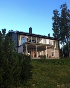 Balcon vitré avec structure blanche sur maison à deux étages avec jardin en pente et ciel dégagé.