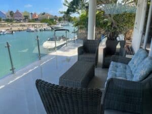 Glasräcke med rostfria stolpar monterat vid altan med utsikt över båtkanal och färgglada hus i tropisk miljö.