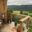 Glasgeländer aus Holz am Blockhaus Glasgeländer mit Holzpfosten und Handlauf auf kleiner Terrasse mit Blumen und Blick auf grüne Berglandschaft.