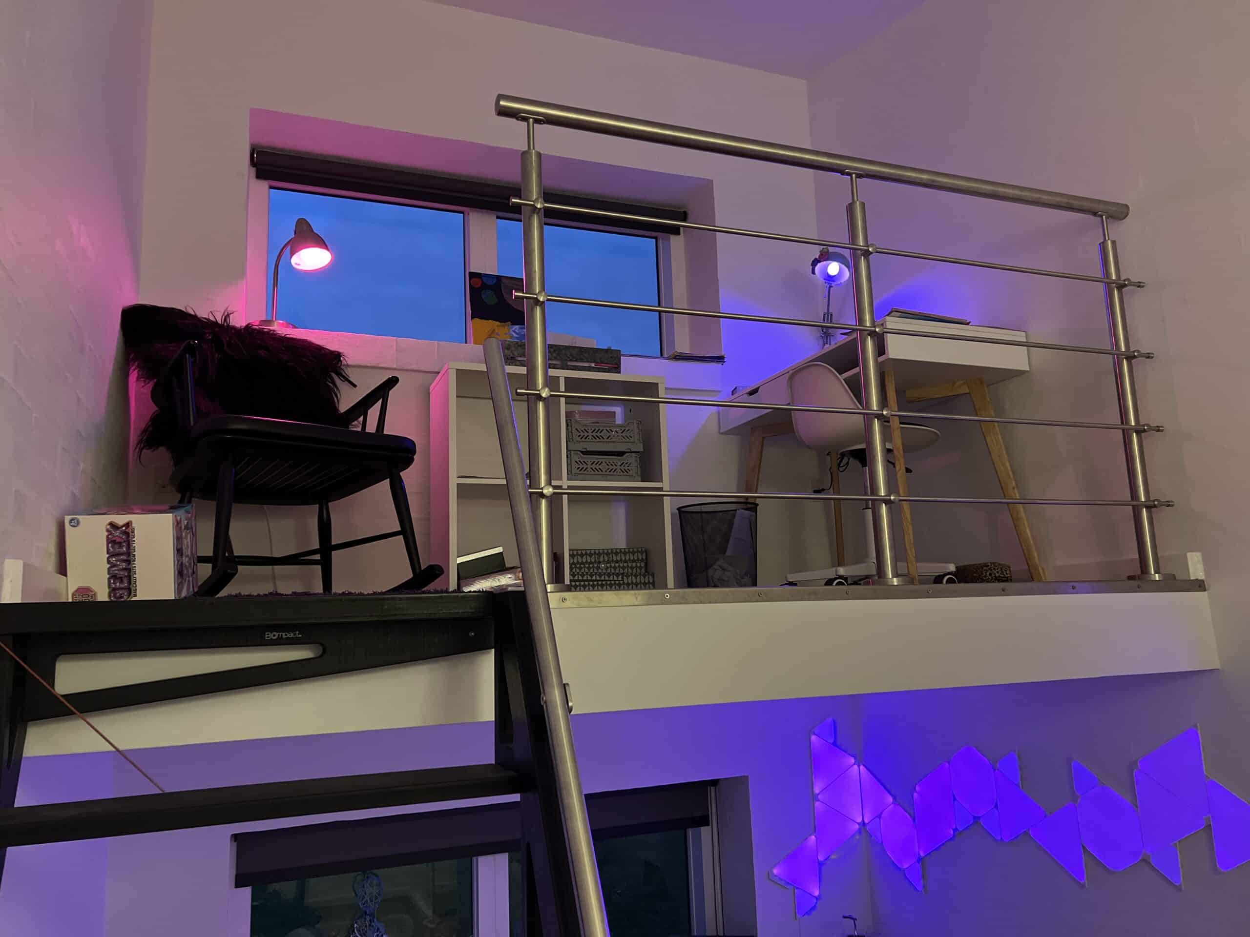 Intérieur avec bureau, chaise et garde-corps horizontal en inox brossé contre un mur blanc et lumière d’ambiance.