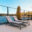 Sort glasværn med søudsigt Sort aluminiumsrækværk med klart glas omkring flisebelagt terrasse med liggestole og panoramaudsigt over sø.