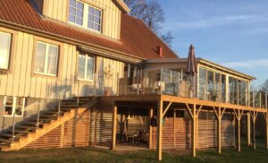 Multi-level deck with glass railing and stairs Clear glass and stainless steel railing along timber stairs and multi-level deck, attached to sunlit garden room façade.