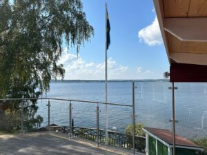 Edelstahl-Glasgeländer auf einer Terrasse mit Blick auf Seelandschaft und österreichische Flagge – ideal für ein Sommerhaus am Wasser.