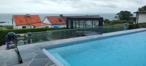 Moderne glashegn omkring poolområde med havudsigt, elegant løsning der beskytter uden at forstyrre omgivelserne.