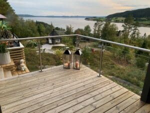 Stainless steel glass balustrade with garden view Timber deck with clear glass and stainless steel railing, facing lake, greenery and decorative garden elements.