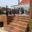 Black Glass Balustrade on Raised Deck Raised composite terrace with black post glass railing surrounding conservatory and barbecue corner in garden setting.