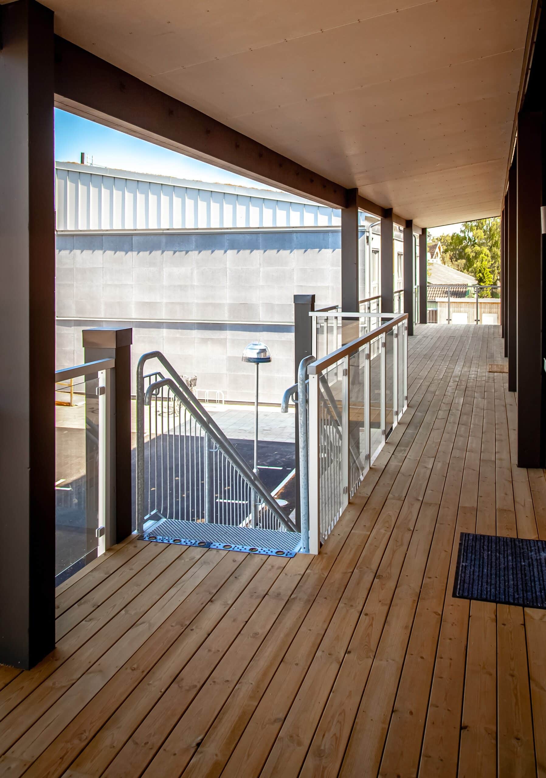 Robust glasräcke med rostfria stolpar och handledare i trä vid entré till offentlig byggnad med trappa och loftgång