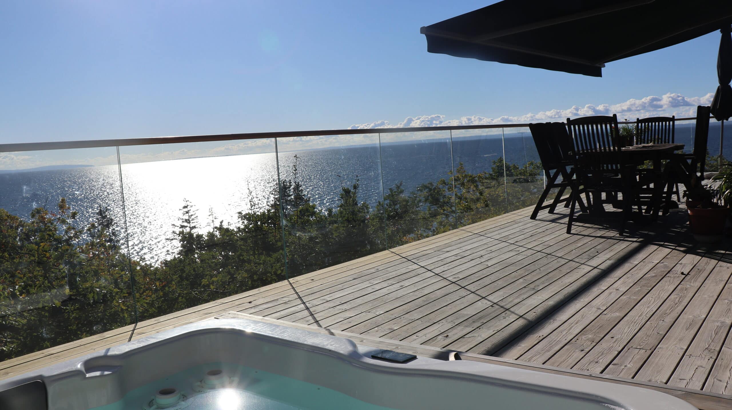 Stolpefritt glassrekkverk på treterrasse med utsikt mot havet – kombinert med spisegruppe og utendørs boblebad
