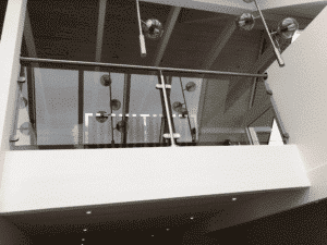 Glasgeländer mit Rauchglas und Handlauf aus Edelstahl, montiert auf einem weißen Loft. Stahlklammern halten das Glas an Ort und Stelle und moderne Lichtquellen spiegeln sich im Glas.