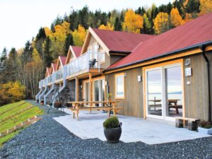 Balcons vitrés sur chalets en bois dans un cadre automnal Rangée de chalets en bois avec garde-corps en verre sur les balcons, entourés de forêt aux couleurs d’automne.
