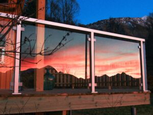 Reflective glass screen with mountain sunset view White aluminium framed glass screen on terrace, reflecting vibrant sunset over distant hills and colourful skies.