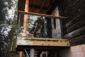 Pfostenfreies Glasgeländer in naturnaher Umgebung Pfostenfreies Glasgeländer auf kleinem Holzbalkon, punktgefasst mit Holzhandlauf, montiert an Blockhaus in waldreicher Umgebung.