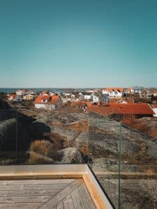 Ausblick durch pfostenfreies Glasgeländer Nahaufnahme einer Ecke eines pfostenfreien Glasgeländers mit Klarglas und Holzrahmen, montiert auf Terrasse mit Blick auf Felsen und Küstenlandschaft.