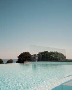 Glasgeländer am Pool mit Meerblick Pfostenfreies Glasgeländer am Infinity-Pool mit Blick auf das Meer und Baumkronen – für ein offenes, luxuriöses Ambiente.
