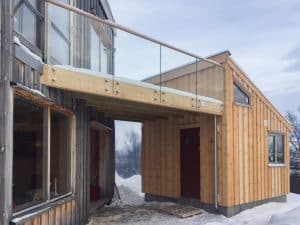 Glasgeländer auf dem Balkon in alpiner Umgebung Pfostenfreies Glasgeländer auf Holz-Balkon in Berglandschaft, mit Holzbefestigung und Holzhandlauf zwischen zwei Holzhäusern im Winter.