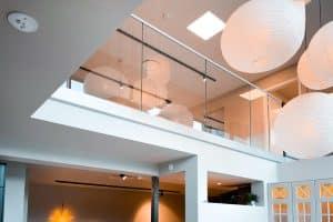 Stilvolles Glasgeländer in öffentlicher Umgebung Modernes, pfostenfreies Glasgeländer montiert in einem öffentlichen Innenraum mit hoher Decke, großen Papierlampen und heller Gestaltung.
