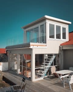 Pfostenfreies Glasgeländer auf dem Balkon Modernes, pfostenfreies Glasgeländer mit Klarglas und Holzsockel, montiert auf einem weißen Haus mit Meeresnähe.